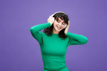 Young cheerful brunette woman with long wavy hair listening to music in headphones and enjoying it...