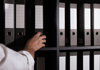 Hand taking folder binder from office shelf. Business documents, files archive concept