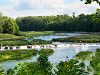 Kuldiga, Latvia - July 31, 2021: Tourists cross the river Vetna along the longest waterfall in Europe Rumba.