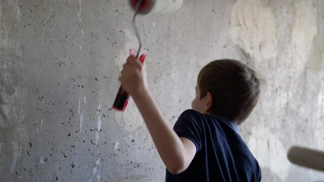 cheerful house renovation, caucasian boy 7-8 years old with a smile holding paint rollers dances against the wall, apartment renovation, wall painting. child renovating the house