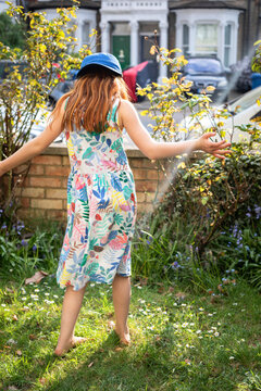 A red headed girl dancing in a garden by herself.