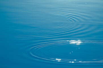 Wave ripple circles on the lake. Blurred transparent blue colored clear calm water surface texture....
