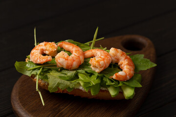 Bruschetta on a fresh baguette with arugula, cream cheese, avocado and shrimp on a wooden board