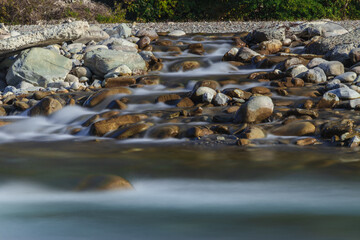 Obraz premium Water flowing over rocks, flowing through rocks. Long exposure time. A long exposition of the river in the Caucasus mountains. The stones in the river are blurred from long exposure.