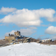Medieval fortress on the hill of the mountain. Ruins of an old castle against a blue sky with clouds. Scenic view of the fortress mountain landscape in winter