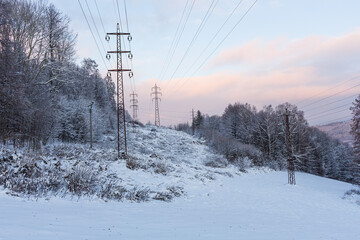 Obraz premium The overhead electric line over blue sky. Electrical wires of power line or electrical transmission line covered by snow in the winter forest.