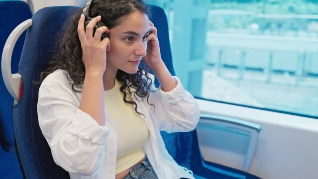 young woman is travelling by train and listening to music by headphones, sitting near window