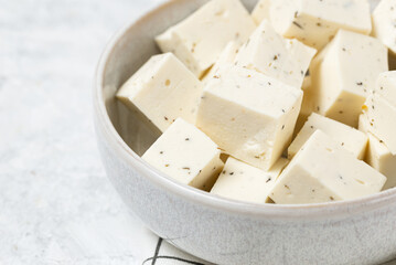 Tofu soy cheese or paneer or feta cheese cubes in a ceramic bowl on a checkered napkin isolated closeup