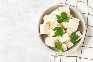 Tofu soy cheese or paneer or feta cheese cubes adding fresh parsley and celery in a ceramic bowl on...