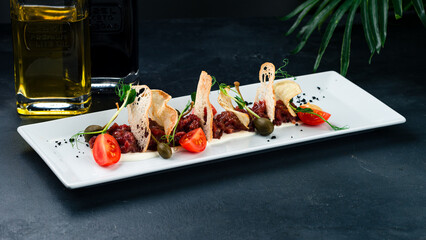 Cold appetizer of beef carpaccio with cherry tomatoes, chips, microgreens, capers and sauce.