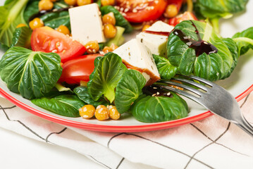 Fresh pak choi salad with tomatoes, chickpeas and feta cheese, poured with sauce and sesame seeds in a plate with a fork close up