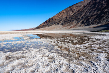 Beautiful landscape of salt flats with water reflection of mountains and blue sky at the Badwater Basin, Death Valley National Park, California, United States.