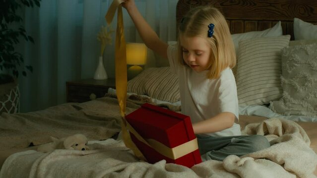 Little small Caucasian daughter child girl kid on bed opening unpacking Christmas New Year birthday gift box confused with wrong unwanted present dissatisfied with empty parcel with nothing inside