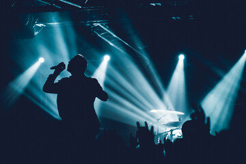 Rock singer on scene in club. Bright stage lighting. Band Blue Silhouette. Vocalist singing to microphone. hand fans during a concert