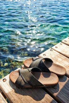 A pair of mens leather sandals on water's edge by sea.
