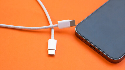 USB type C port cable for charging to the smartphone on orange background. EU law to force USB-C...