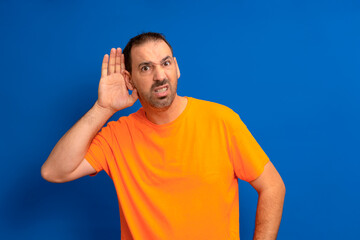 Listening man holds his hand near his ear on a blue background. Handsome man trying to listen to someone's conversation