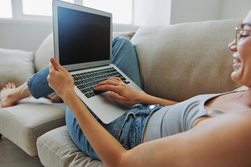 Fototapeta premium Teenage girl freelancer with laptop sitting on couch at home smiling in home clothes and glasses with short haircut, lifestyle with no filters, free copy space