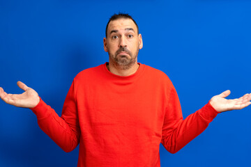 Caucasian bearded man isolated on blue background doubting and shrugging in questioning gesture