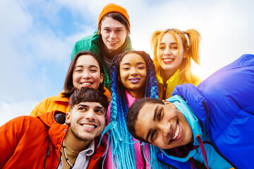 Multiracial group of young happy friends wearing colorful winter jackets meeting outdoors in...