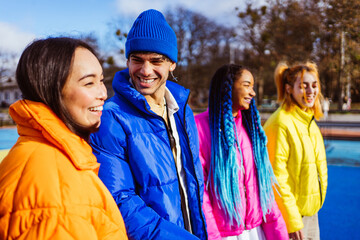 Multiracial group of young happy friends wearing colorful winter jackets meeting outdoors in winter, concepts about youth generation, millennials, teenage and students social gathering