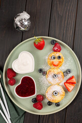 Cheesecakes are laid out in the shape of a Snowman, decorated with berries, sprinkled with powdered sugar, with toppings of berry jam and sour cream