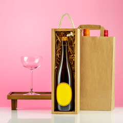 Eco friendly wine shop, bar winery or wine delivery concept. Mockup of bottle of champagne in a wooden box with wine glass and bottles of wine in paper bag on pink background. Ecologic packaging