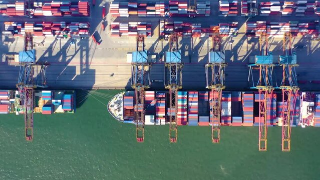 Aerial drone video of a big container cargo vessel docked being loaded at the city to port
