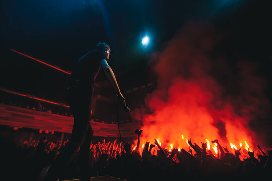Band red silhouette crowd. Popular singer on stage in front of crowd on scene in night club. Bright stage lighting. Crowded dance floor. People get wild on concert.  Dangerous red fireworks in crowd.