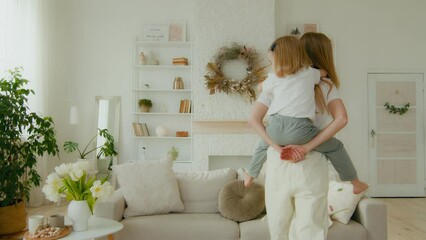 Little small cute girl daughter sitting piggyback at mother piggy back mom rotate around kid whirl child having fun play funny game active at home living room. Caucasian family mummy and baby playing