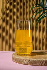 A glass of juice with ice on the background of the shadow of a palm leaf. Refreshing drink at the resort
