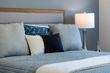 Relaxing bedroom scene of bed with blue and gray linens, knit blanket, side lamp and blue painted wall.