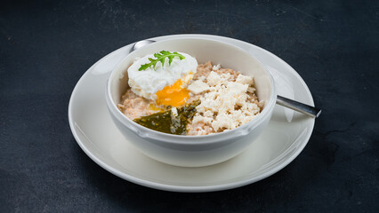English breakfast oatmeal porridge with poached egg, goat cheese and pesto sauce.