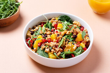 Healthy salad with spelt, oranges, pomegranate seeds. greens and nuts on light background, minimal style