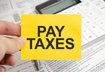 Text PAY TAXES on a business card lying calculator and tax forms