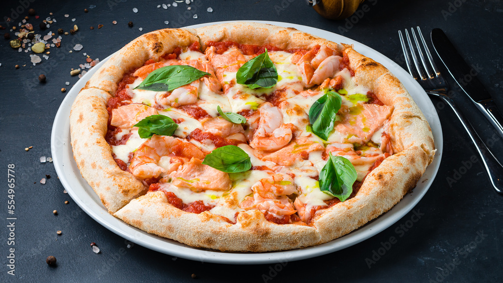 Wall mural Italian pizza with shrimp, salmon, mozzarella, tomato sauce, basil on a thick dough with spices.