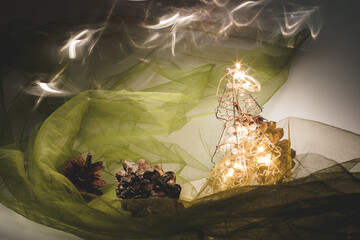 Christmas and New Year's card with a small artificial tree and cones on a table with a colorful background in which lights shine, creating a bokeh background.