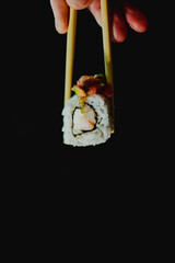 Sushi roll held by chopsticks on black background