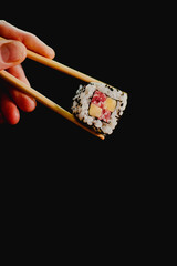 Sushi roll held by chopsticks on black background