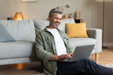 Smiling old caucasian male typing on computer, chatting on social media, watching video and playing...