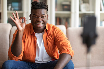 Positive cool black guy vlogger streaming from home, using phone