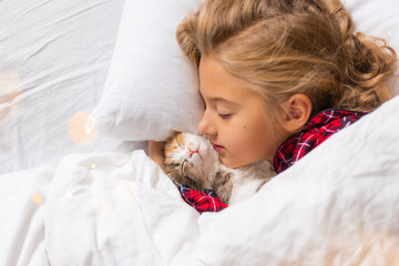 a cute little girl is sleeping sweetly at home in a rabbit with a kitten. White cotton bed linen....