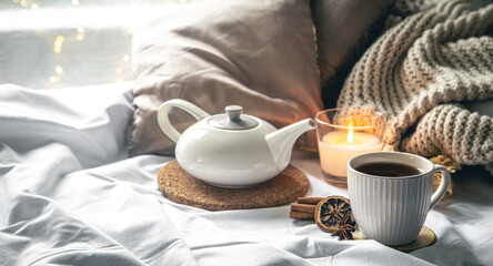 Cozy composition with a cup of tea, a teapot and a candle in the bed.