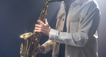 Male musician on stage plays the saxophone dark with smoke.