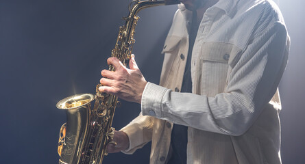 Fototapeta premium Male musician on stage plays the saxophone dark with smoke.