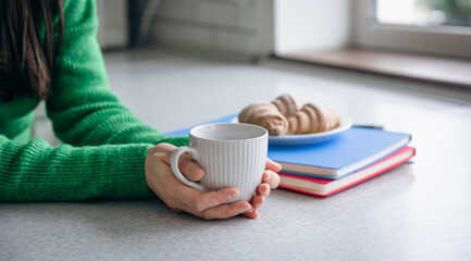 Cup of coffee in female hands in the kitchen, coffee break concept.
