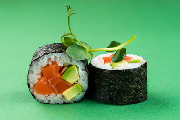 Sushi rolls with salmon, avocado, rice and nori on green background.