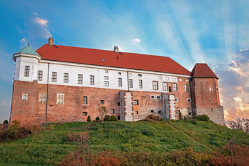 Widok na Zamek Królewski w Sandomierzu w Polsce, delikatnie oświetlony promieniami zachodzącego słońca.
