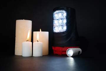 Electric flashlights and burning candles on a black background, alternative sources of light and...