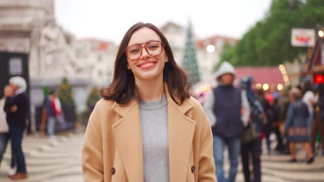 Woman in eyeglasses dressed coat walk city square market looking camera and smile. European female person in glasses walking city warm winter day. 
